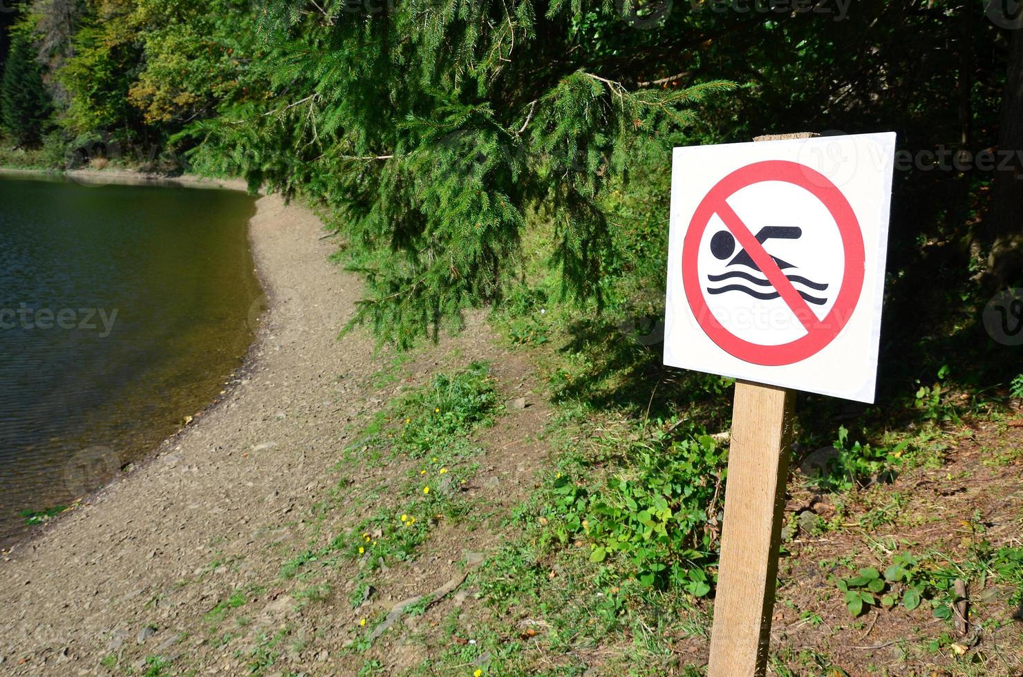 un pilar con un cartel que indica la prohibición de nadar. el letrero muestra a una persona flotante tachada foto