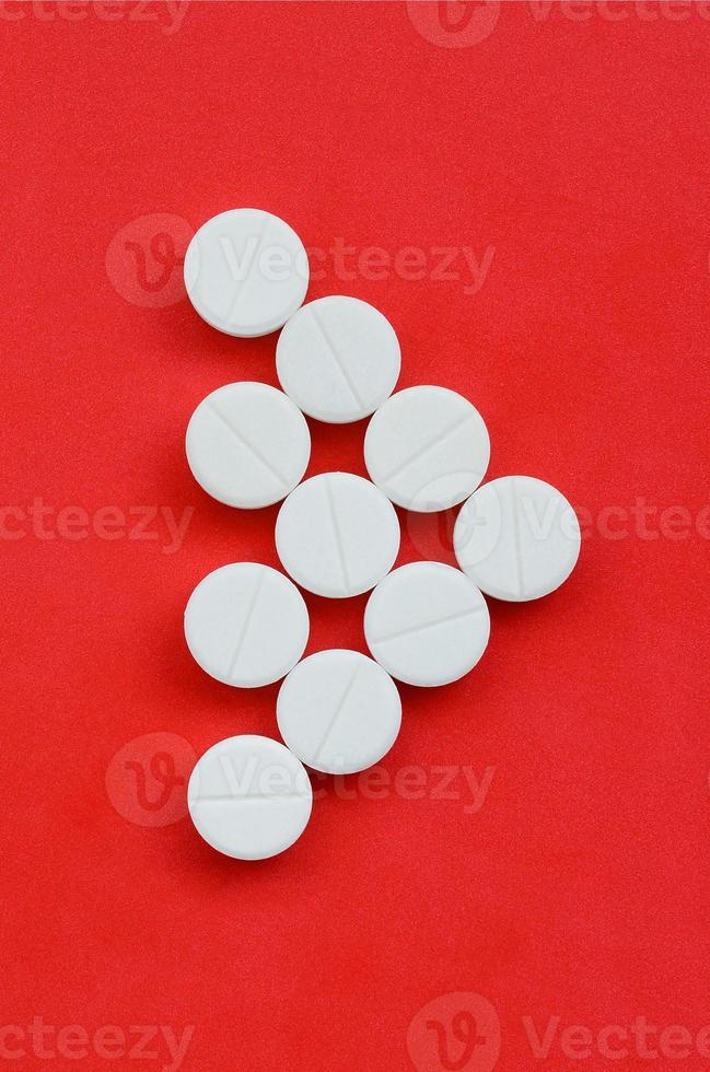 Several white tablets lie on a bright red background in the form of a triangular arrow. Background image on medicine and pharmaceutical topics photo