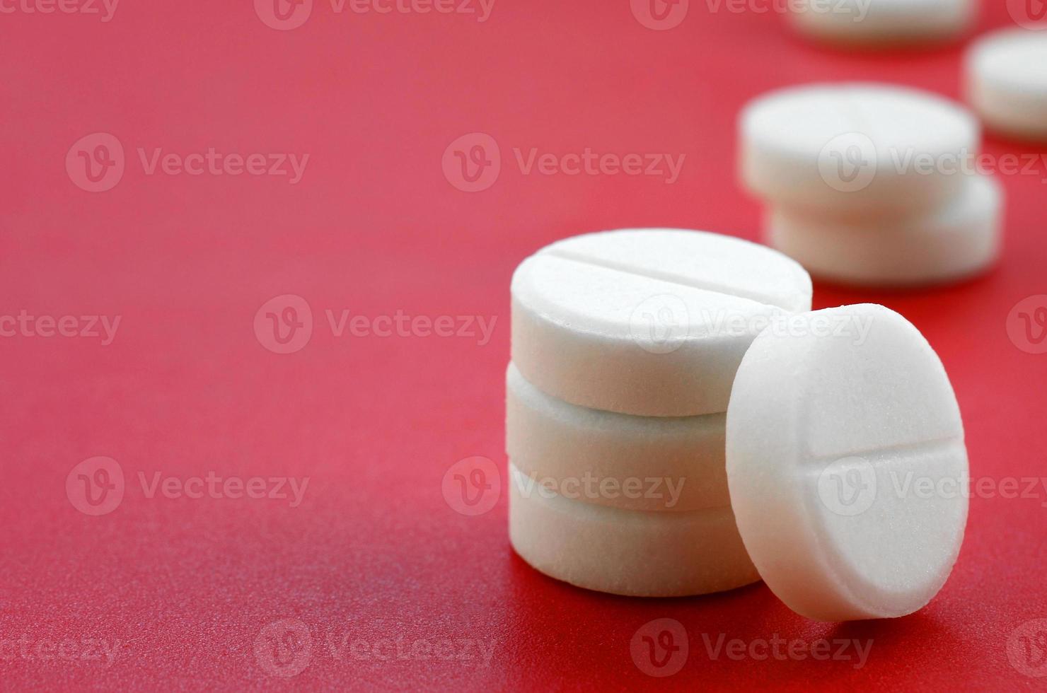 A few white tablets lie on a bright red background surface. Background image on medical and pharmaceutical topics photo