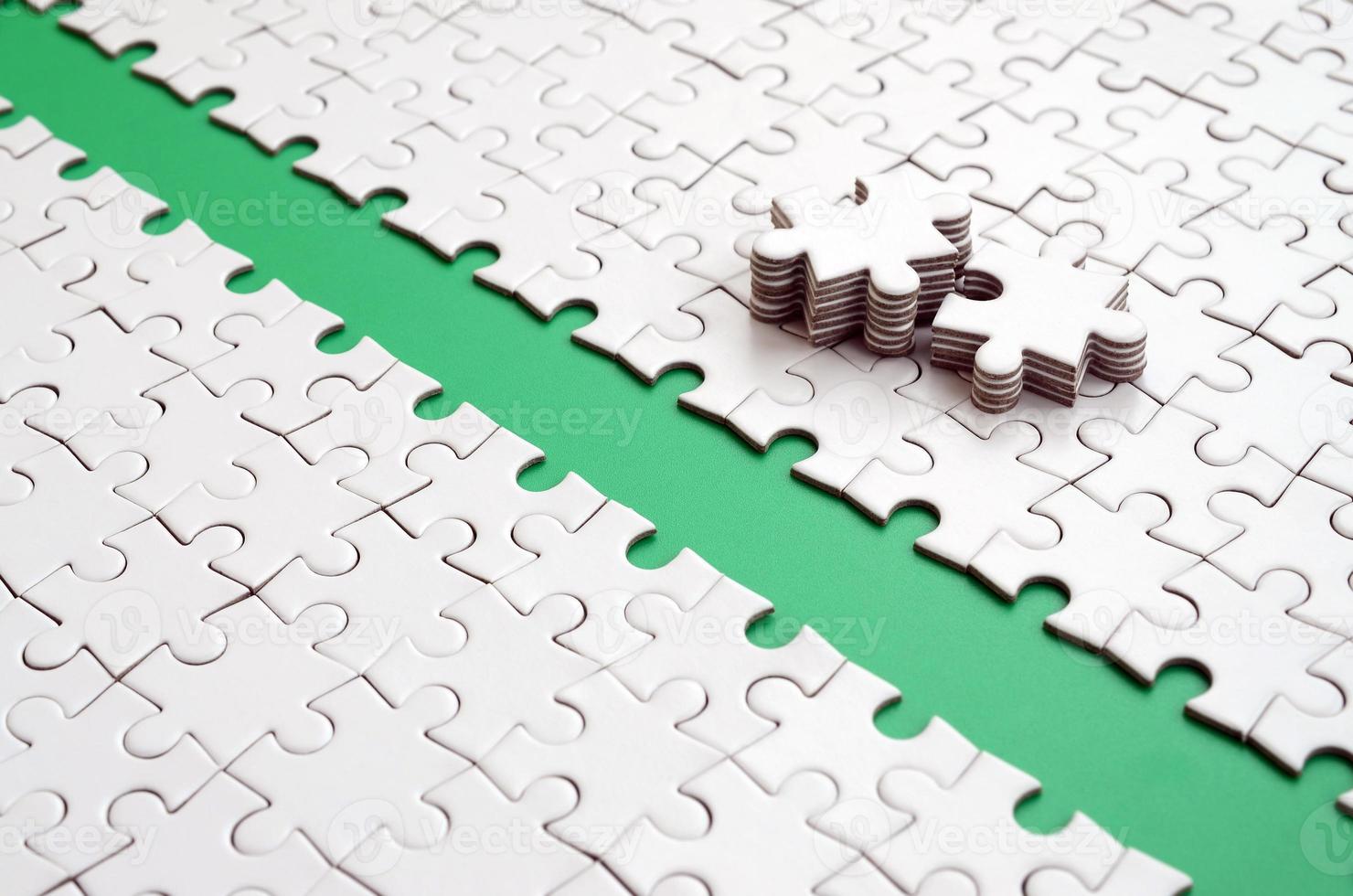 The green path is laid on the platform of a white folded jigsaw puzzle. The missing elements of the puzzle are stacked nearby. Texture image with space for text photo