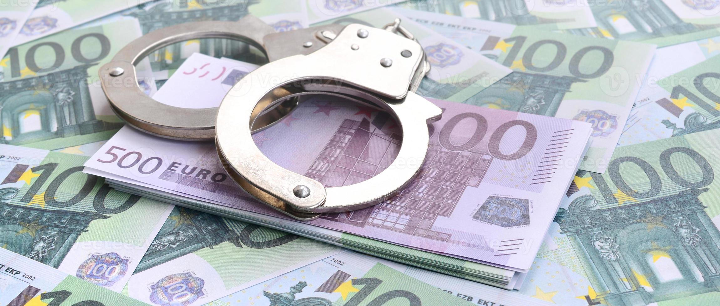 Police handcuffs lies on a set of green monetary denominations of 100 euros. A lot of money forms an infinite heap photo
