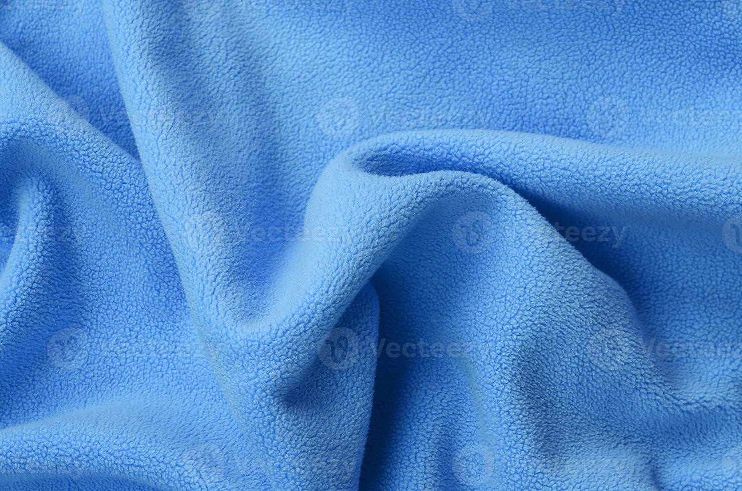 The blanket of furry blue fleece fabric. A background of light blue soft plush fleece material with a lot of relief folds photo