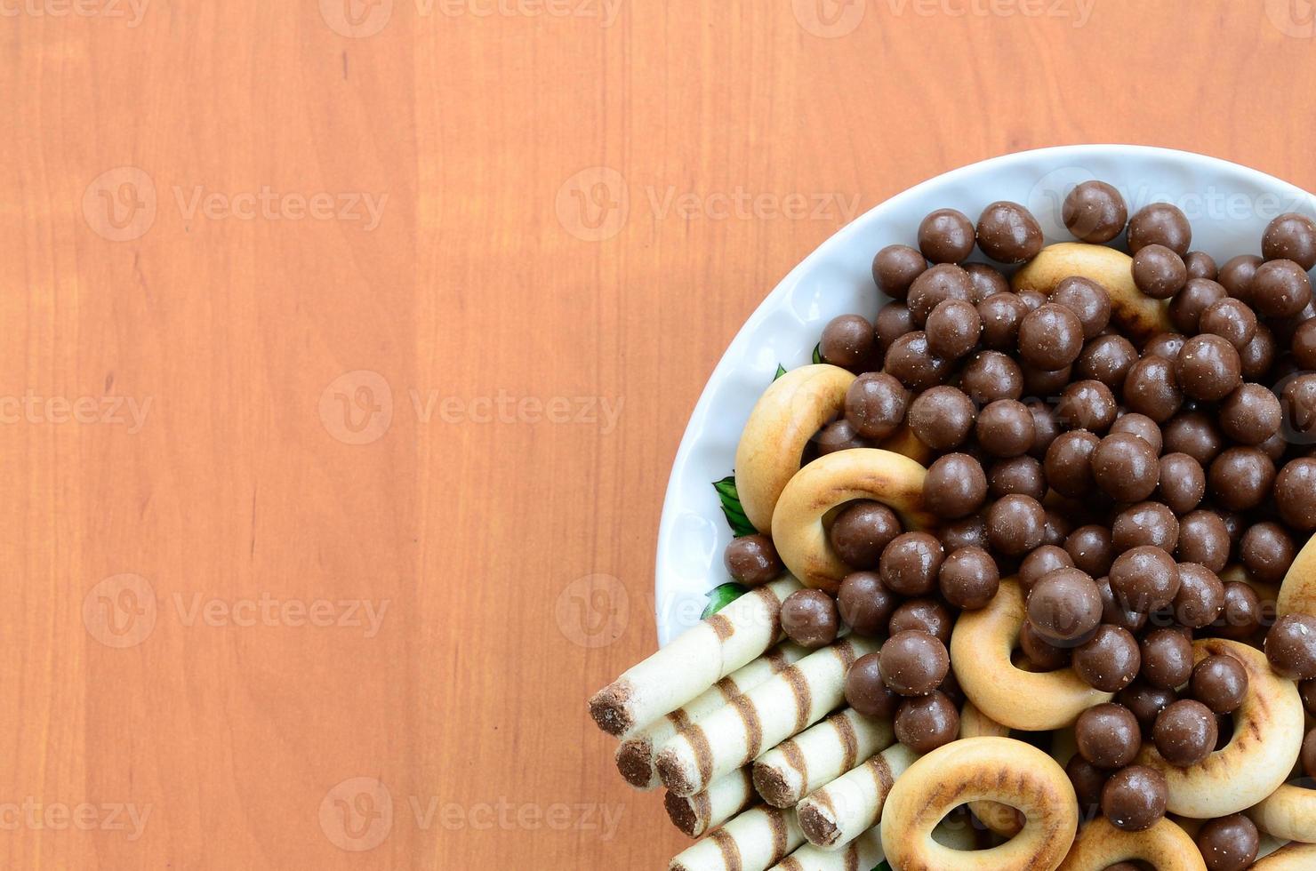 Crispy tubules, chocolate melting balls and bagels lie in a white plate on a wooden table. Mix of various sweets photo
