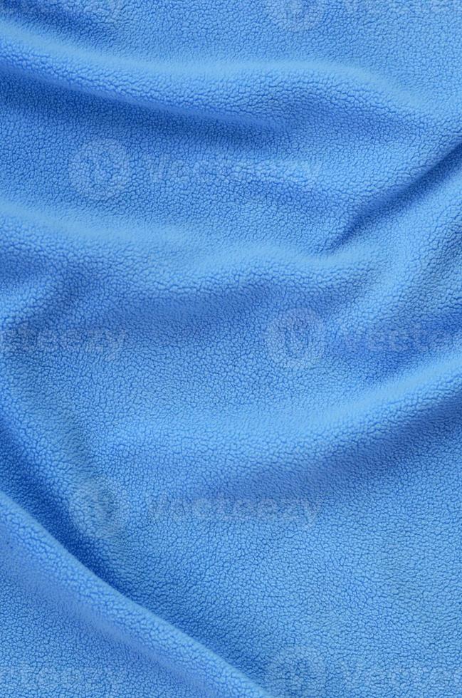The blanket of furry blue fleece fabric. A background of light blue soft plush fleece material with a lot of relief folds photo