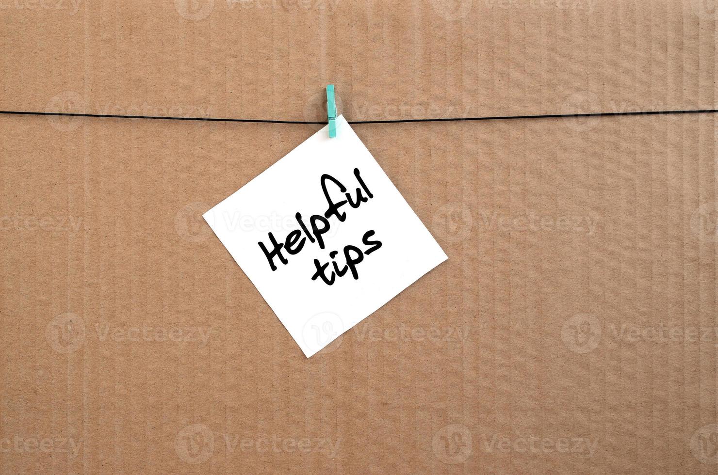 Helpful tips. Note is written on a white sticker that hangs with a clothespin on a rope on a background of brown cardboard photo