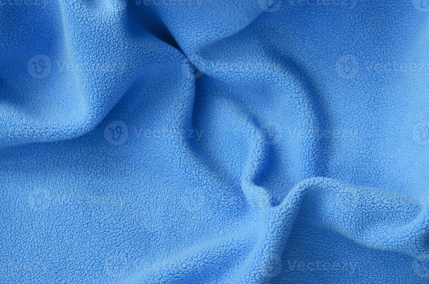 The blanket of furry blue fleece fabric. A background of light blue soft plush fleece material with a lot of relief folds photo