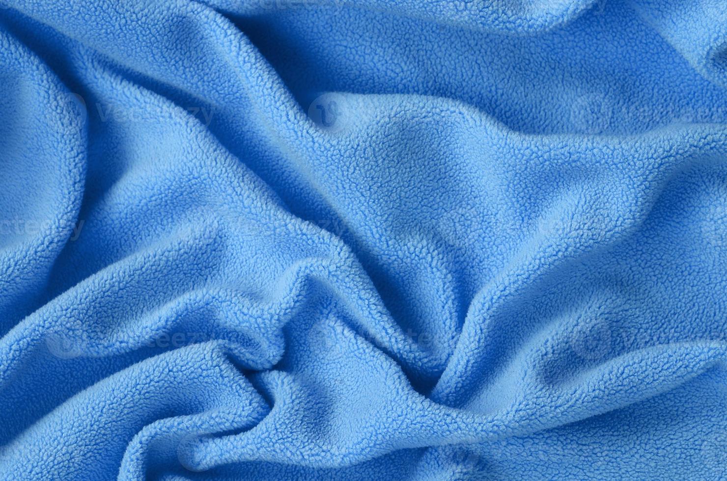 The blanket of furry blue fleece fabric. A background of light blue soft plush fleece material with a lot of relief folds photo
