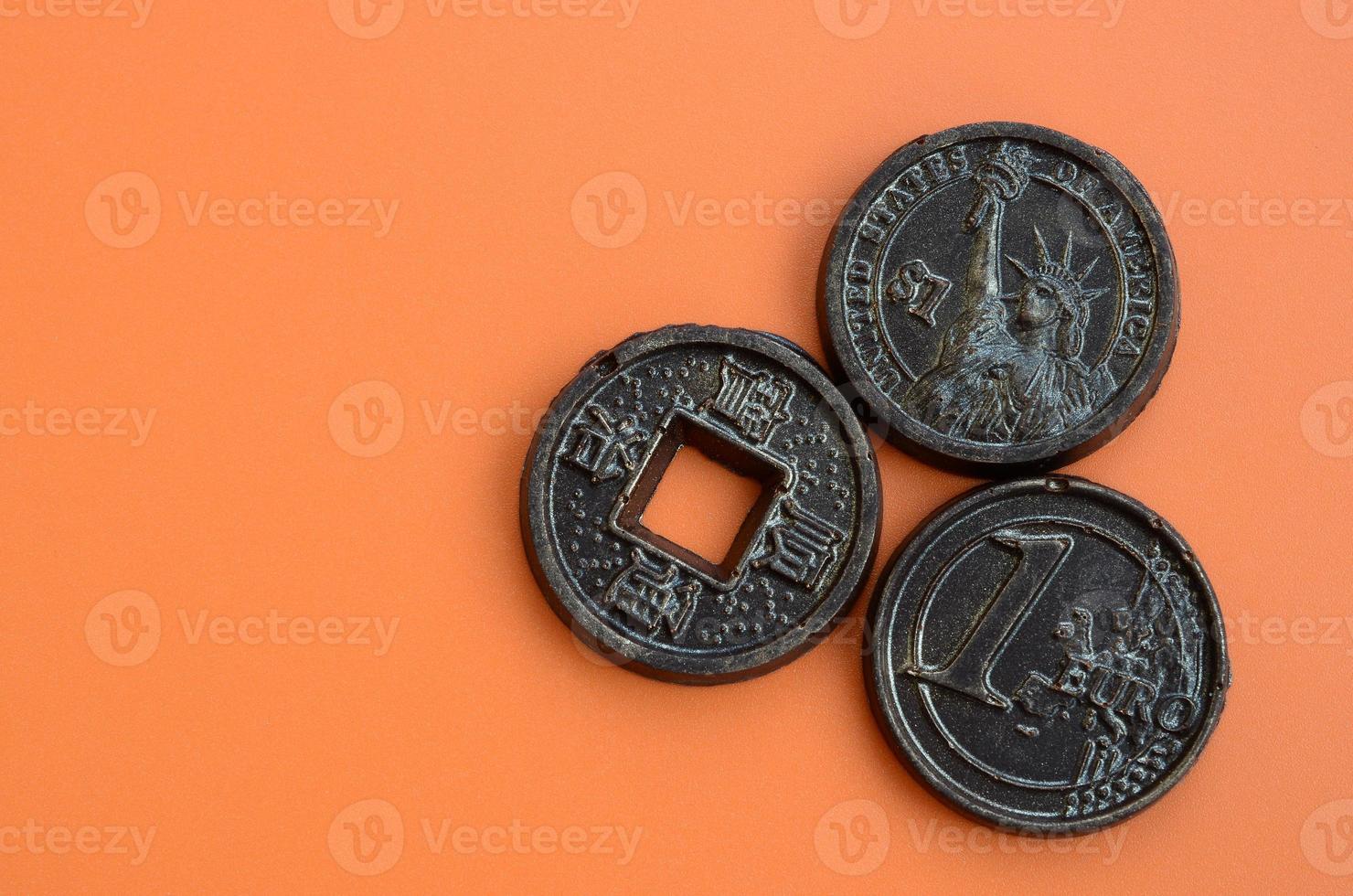 Three chocolate products in the form of Euro, USA and Japan coins lie on an orange plastic background. A model of cash coins in an edible form photo