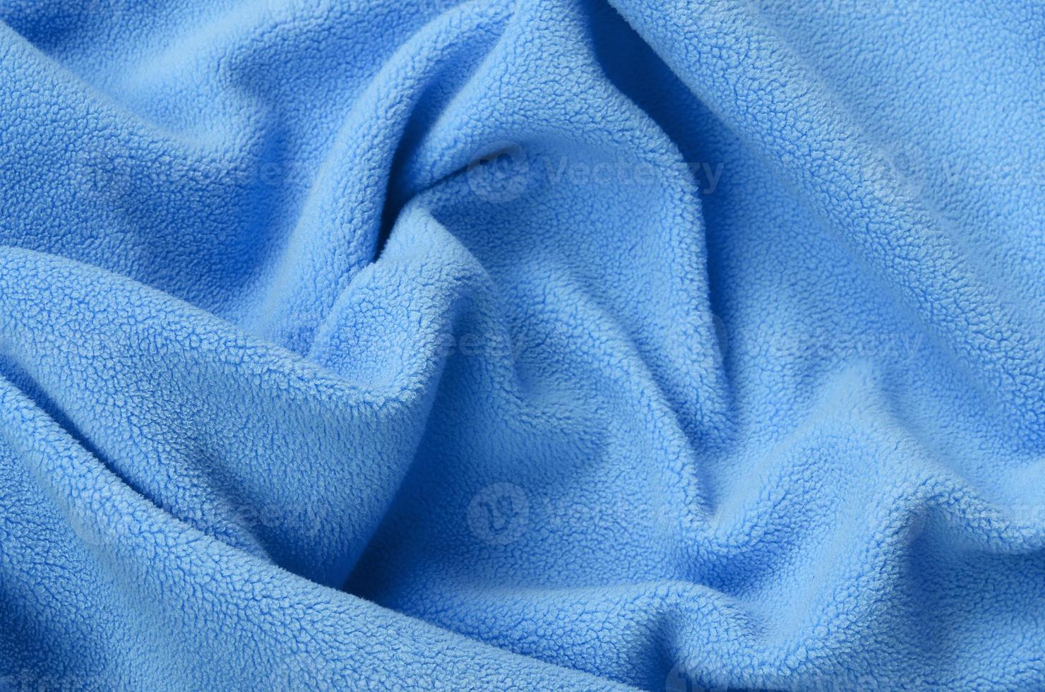 The blanket of furry blue fleece fabric. A background of light blue soft plush fleece material with a lot of relief folds photo