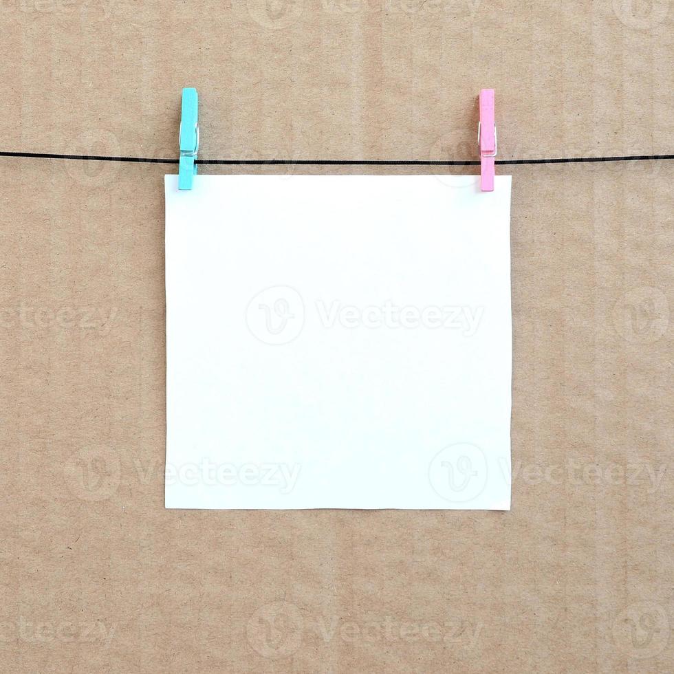 White blank card on rope on a brown cardboard background. Creative reminder, small sheet of paper on wooden clothespin, memo backdrop photo