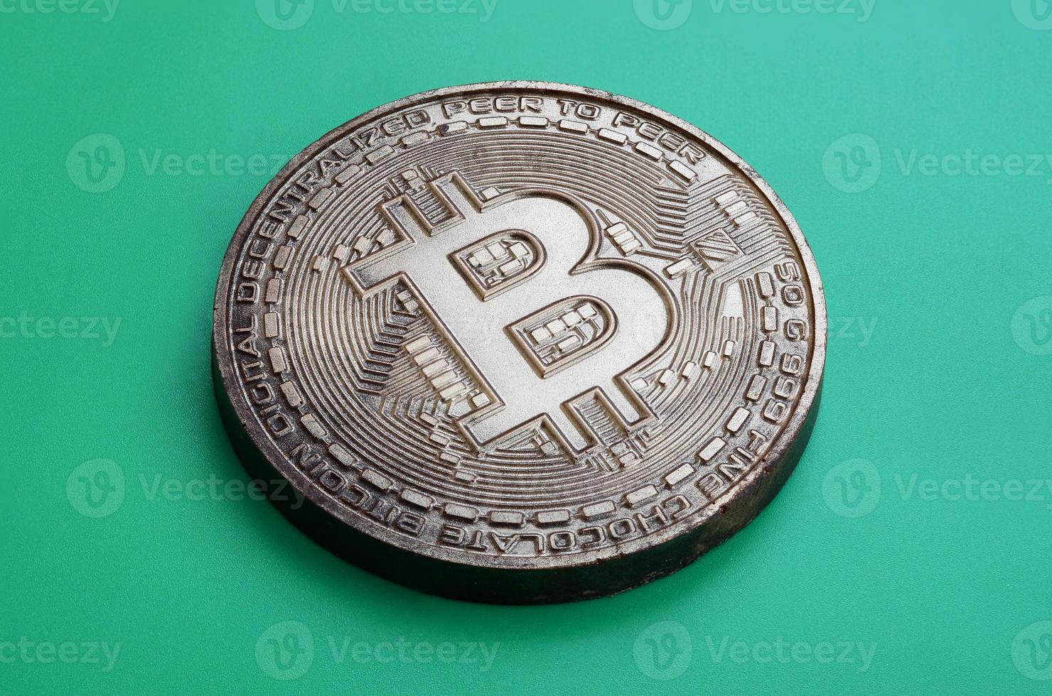 Chocolate product in the form of physical bitcoin lies on a green plastic background. Model of the crypto currency in the edible form photo