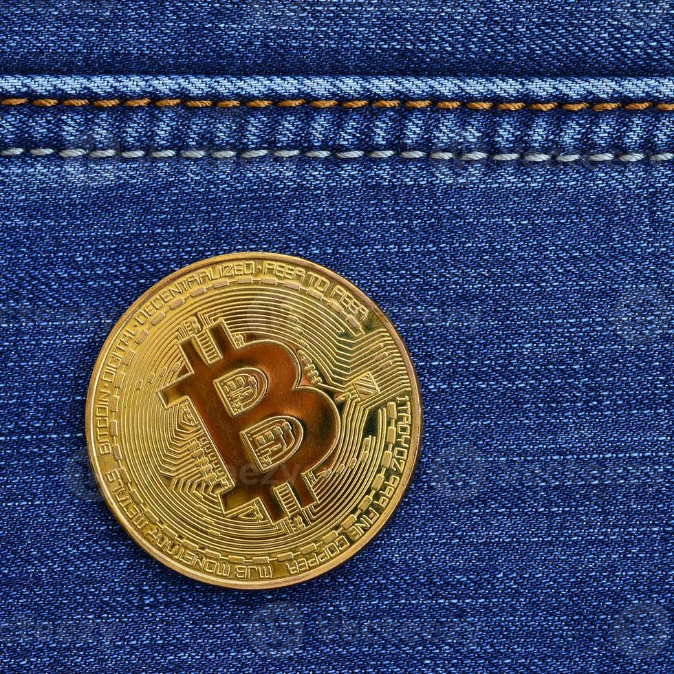 Golden Bitcoin lies on a blue jeans fabric. New virtual money. New crypto currency in the form of the coins photo
