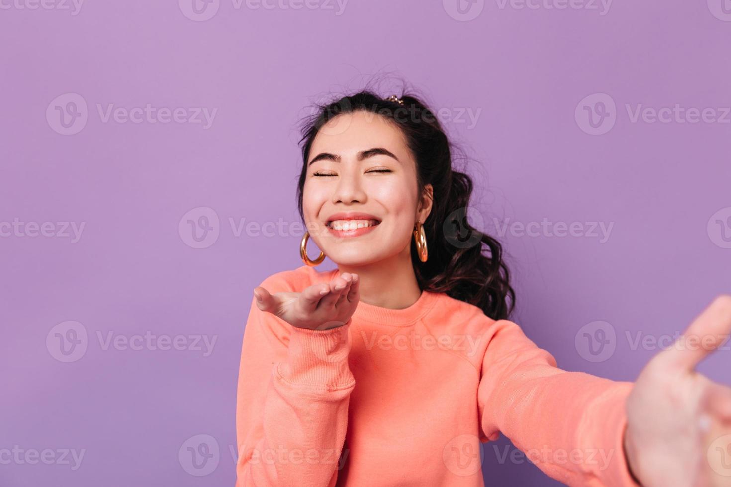 Blithesome chinese girl sending air kiss at camera. Studio shot of smiling asian female model takin photo