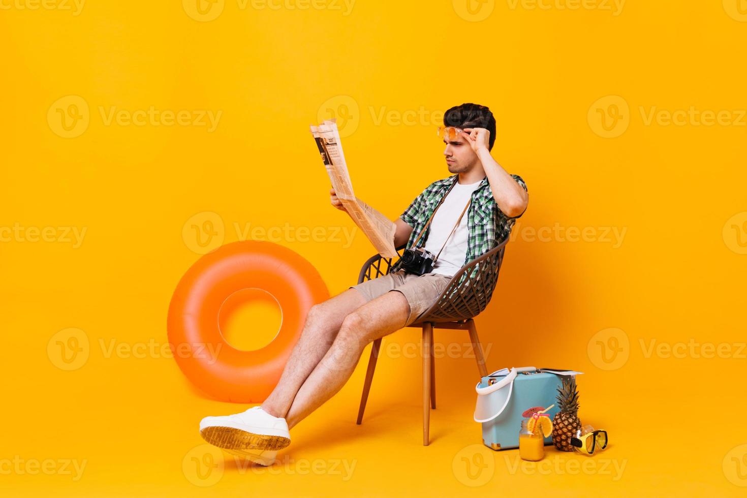el hombre vestido de verano se quita las gafas y lee el periódico. retrato de chico sobre fondo naranja con foto