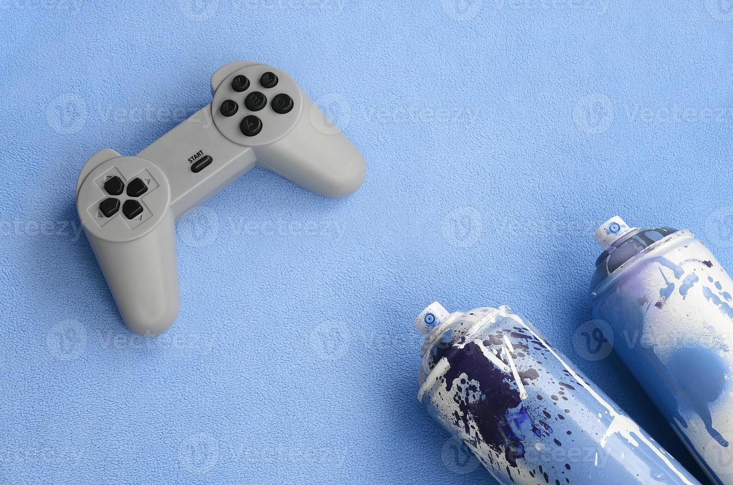 concepto de estilo de vida de adolescentes y jóvenes. joystick y dos latas de aerosol se encuentran sobre la manta de tela de lana azul peluda. controladores para videojuegos y latas de pintura sobre un fondo de material de vellón de felpa foto