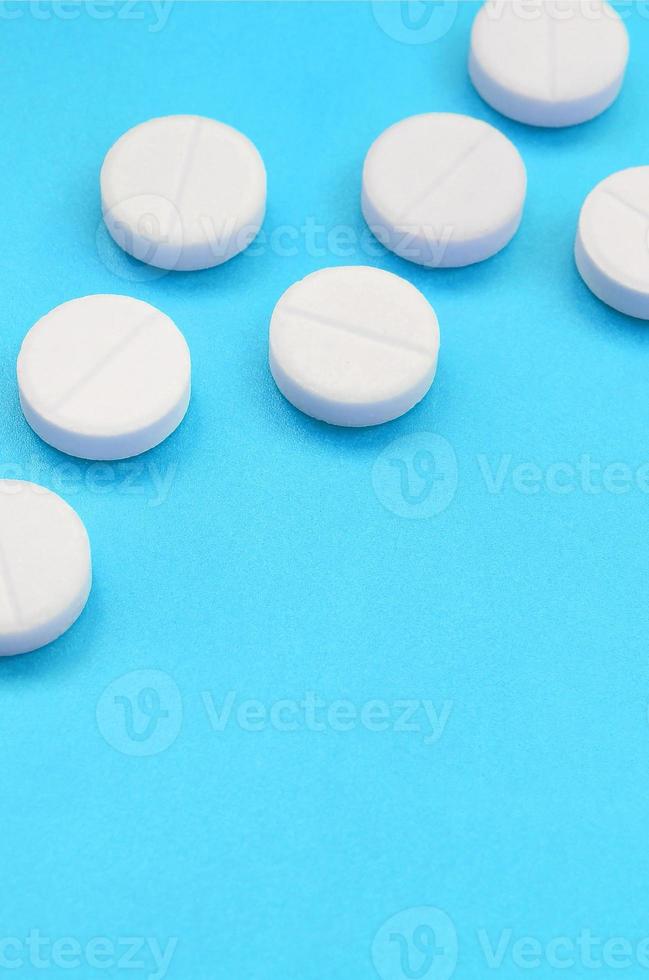 A few white tablets lie on a bright blue background surface. Background image on medical and pharmaceutical topics photo