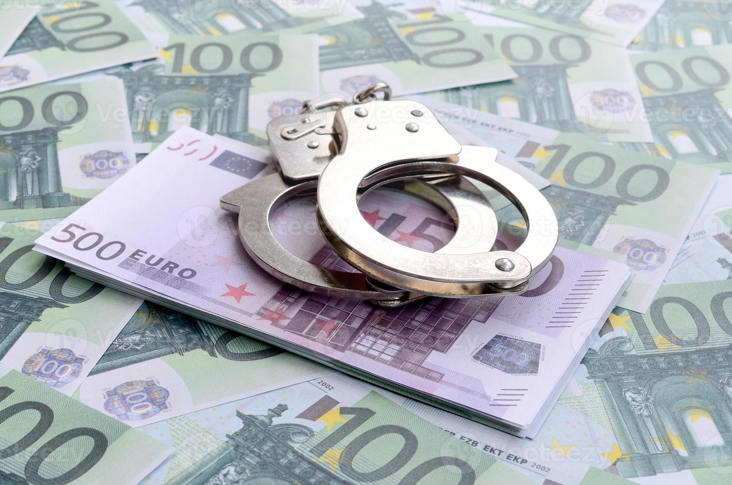 Police handcuffs lies on a set of green monetary denominations of 100 euros. A lot of money forms an infinite heap photo