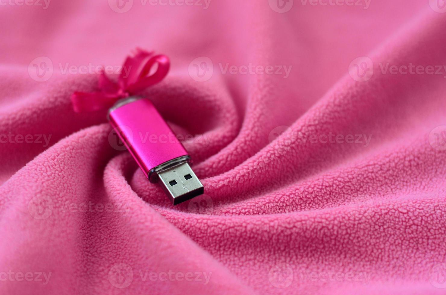 Brilliant pink usb flash memory card with a pink bow lies on a blanket of soft and furry light pink fleece fabric with a lot of relief folds. Memory storage device in women's design photo