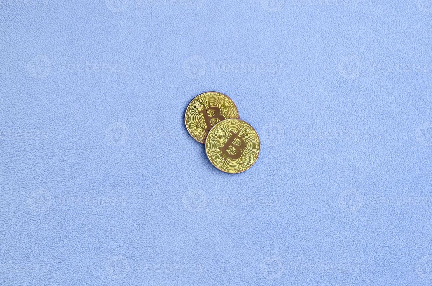 Two golden bitcoins lies on a blanket made of soft and fluffy light blue fleece fabric. Physical visualization of virtual crypto currency photo