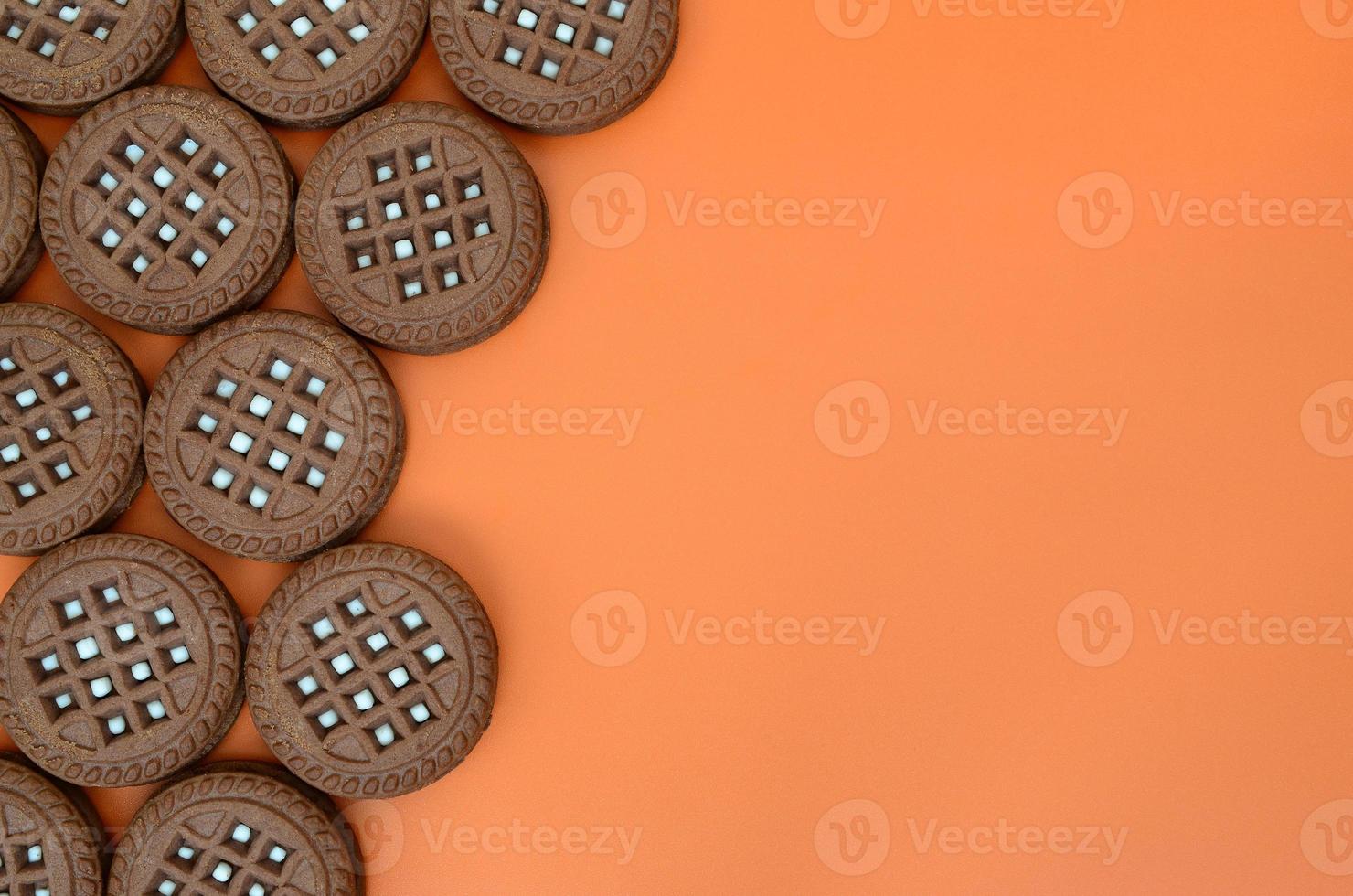 Detailed picture of dark brown round sandwich cookies with coconut filling on an orange surface. Background image of a close-up of several treats for tea photo