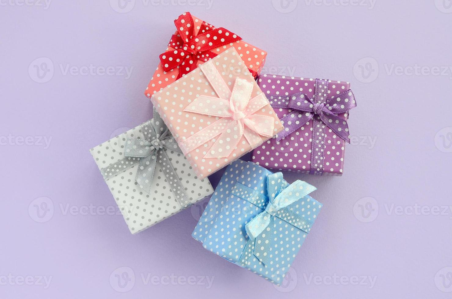 Pile of a small colored gift boxes with ribbons lies on a violet background. Minimalism flat lay top view photo