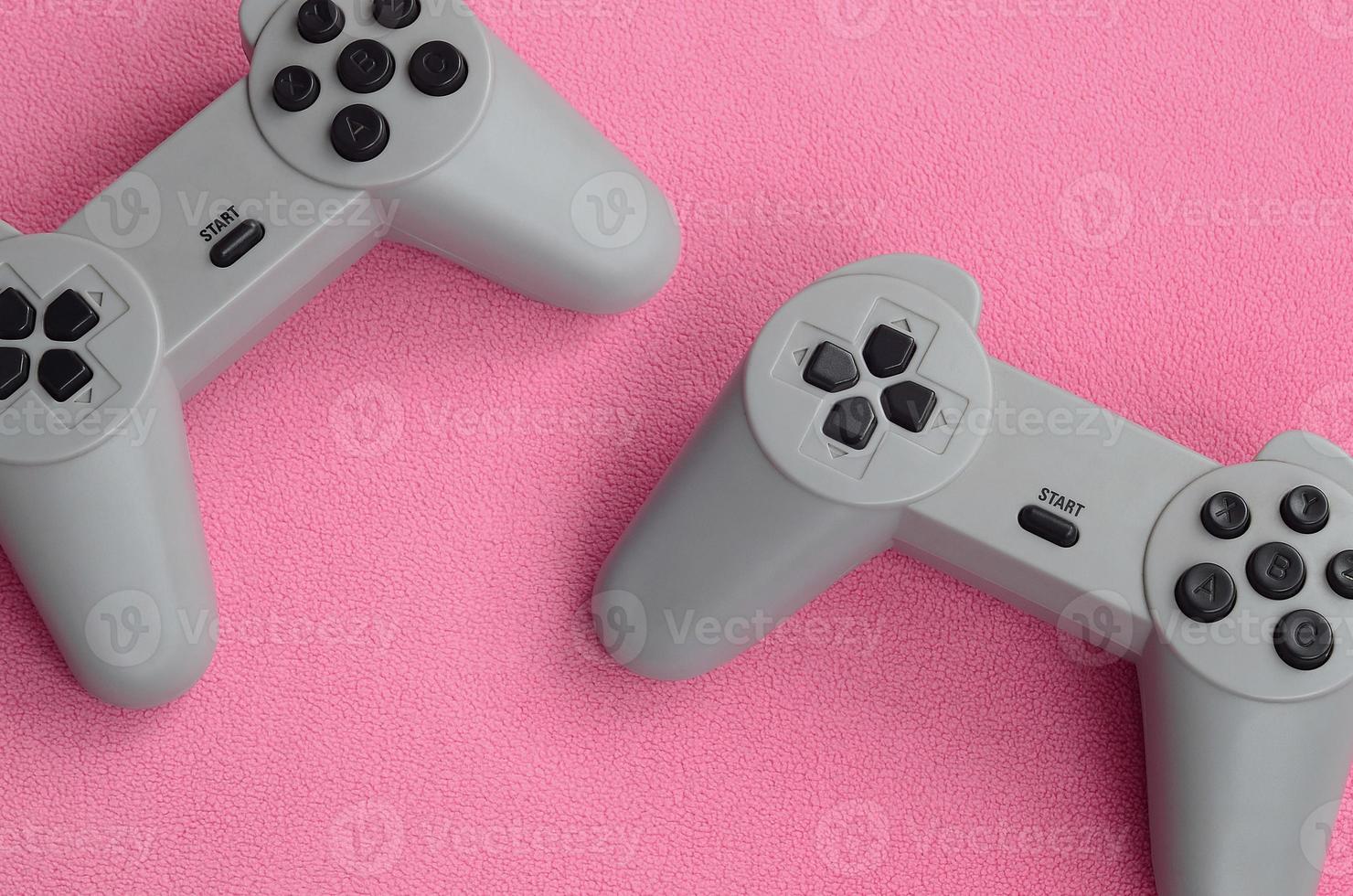 concepto de juegos. dos joysticks de almohadilla se encuentran sobre la manta de tela de lana rosa peluda. controladores para videojuegos en una textura de fondo de material de felpa suave rosa claro foto