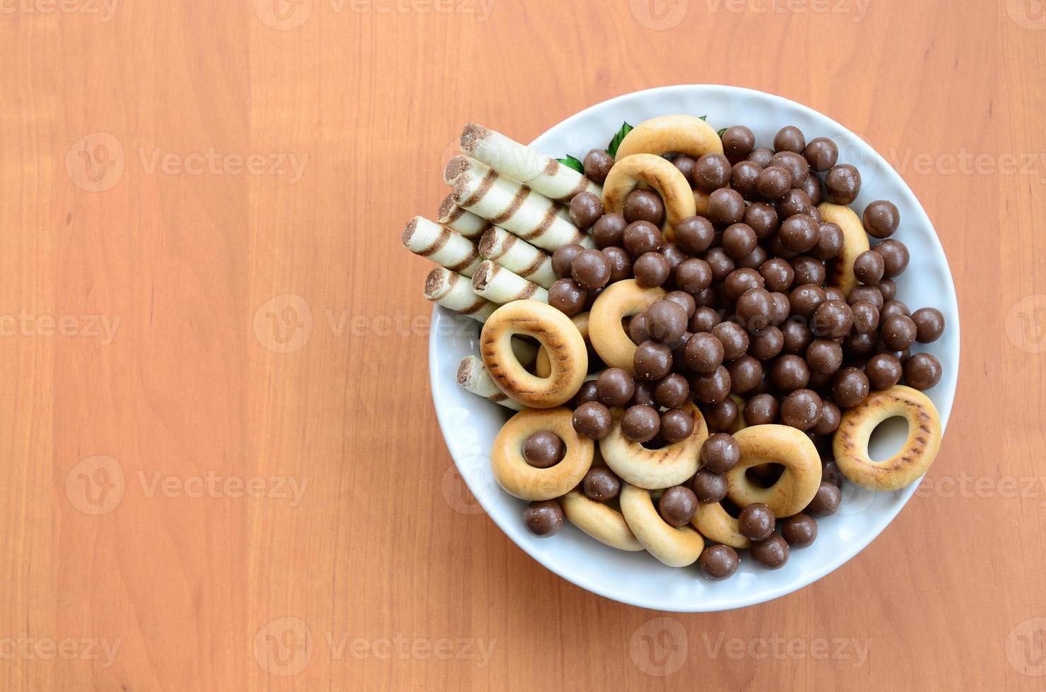 Crispy tubules, chocolate melting balls and bagels lie in a white plate on a wooden table. Mix of various sweets photo