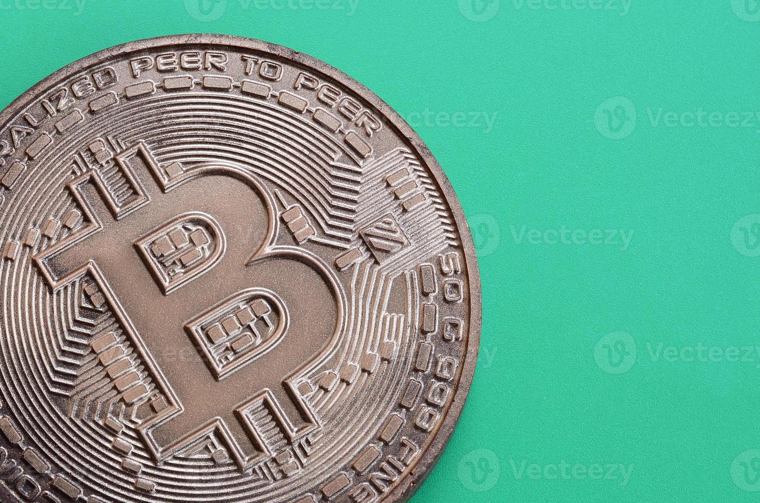 Chocolate product in the form of physical bitcoin lies on a green plastic background. Model of the crypto currency in the edible form photo