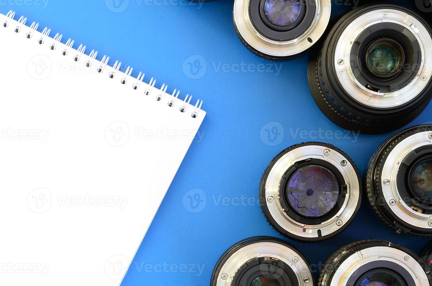 Several photographic lenses and white notebook lie on a bright blue background. Space for text photo