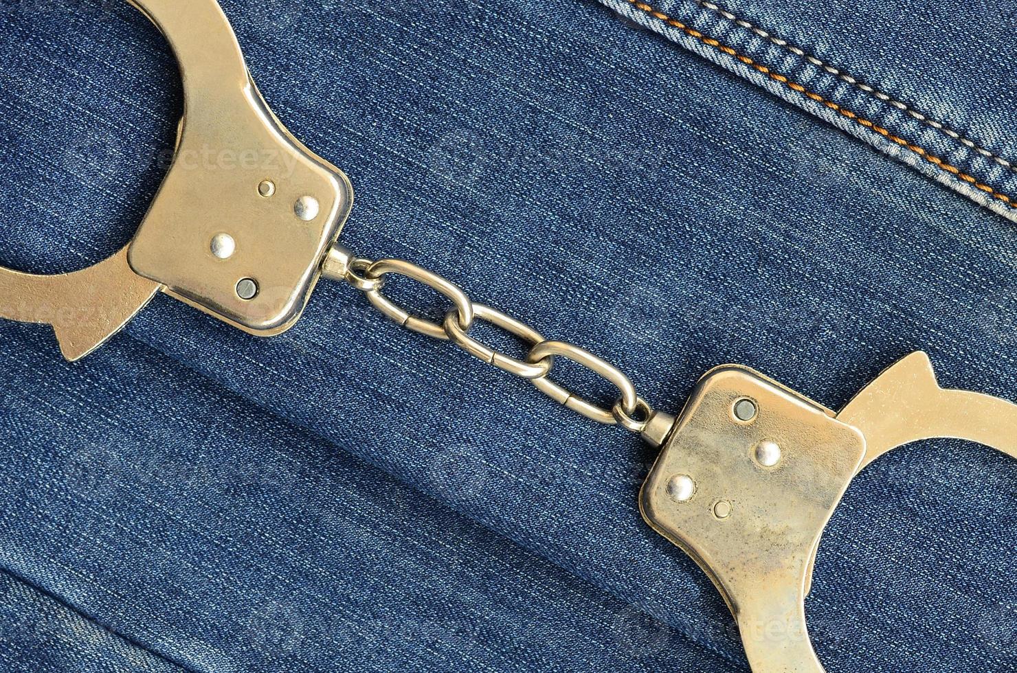 Police steel handcuffs lying on dark blue jeans background photo