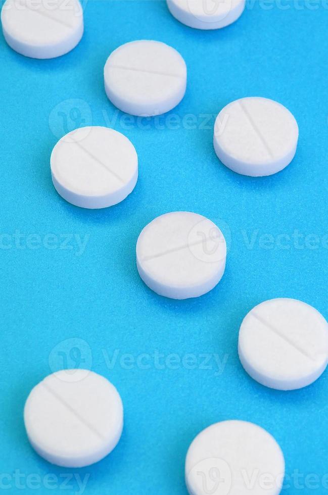 A few white tablets lie on a bright blue background surface. Background image on medical and pharmaceutical topics photo