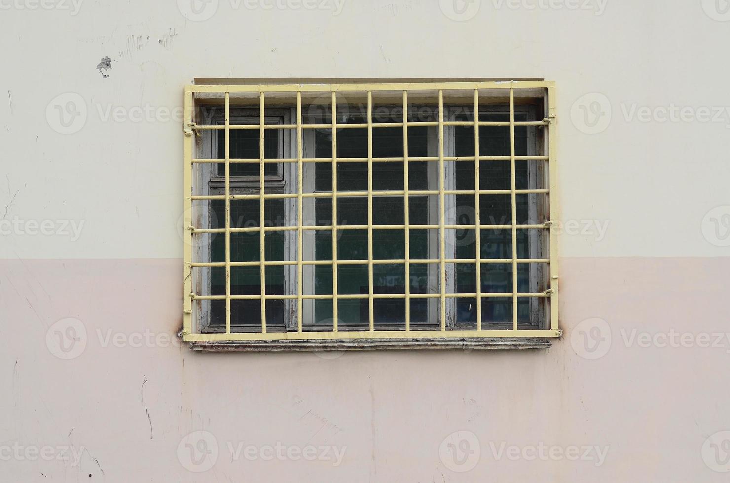 The texture of the wall of a residential building with a window that is protected by a metal grill. Old method of protecting housing from robbers photo