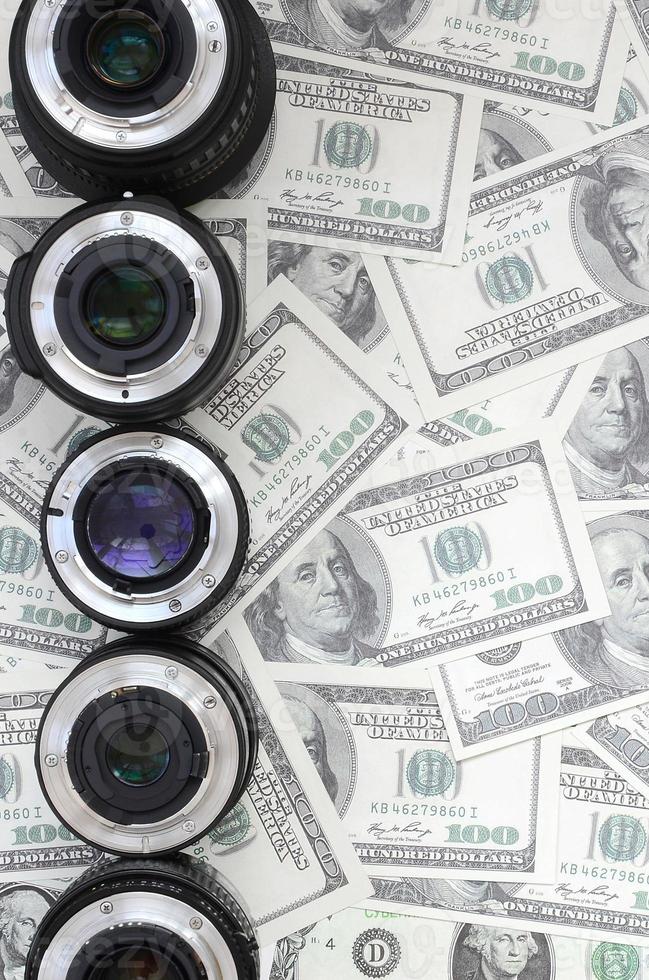 A few photographic lenses lies on the background of a lot of dollar bills. Space for text photo