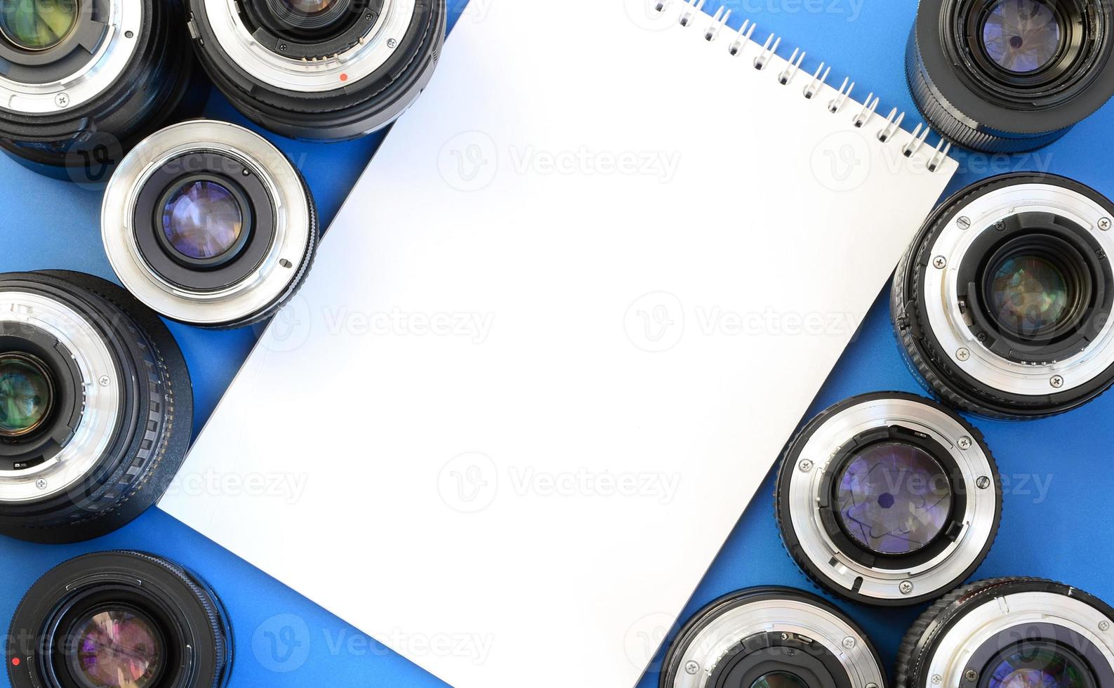 Several photographic lenses and white notebook lie on a bright blue background. Space for text photo