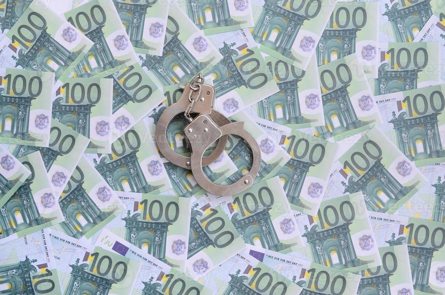 Police handcuffs lies on a set of green monetary denominations of 100 euros. A lot of money forms an infinite heap photo