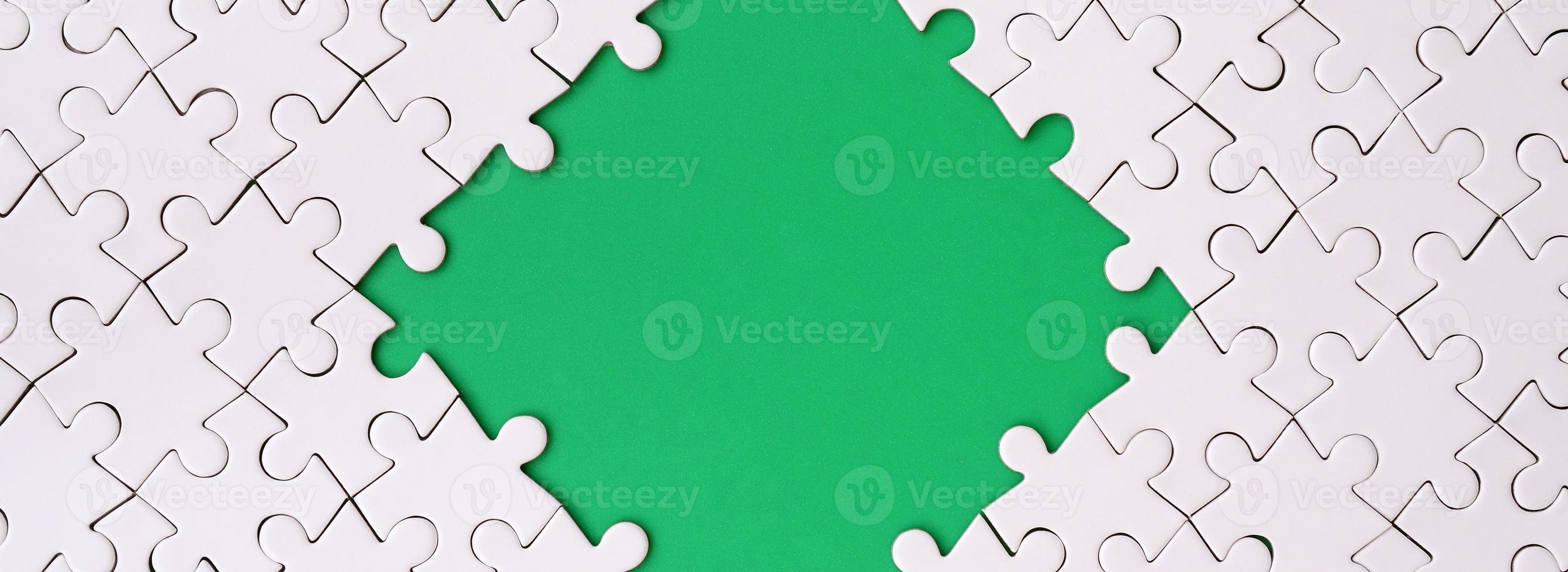 Framing in the form of a rhombus, made of a white jigsaw puzzle around the green space photo