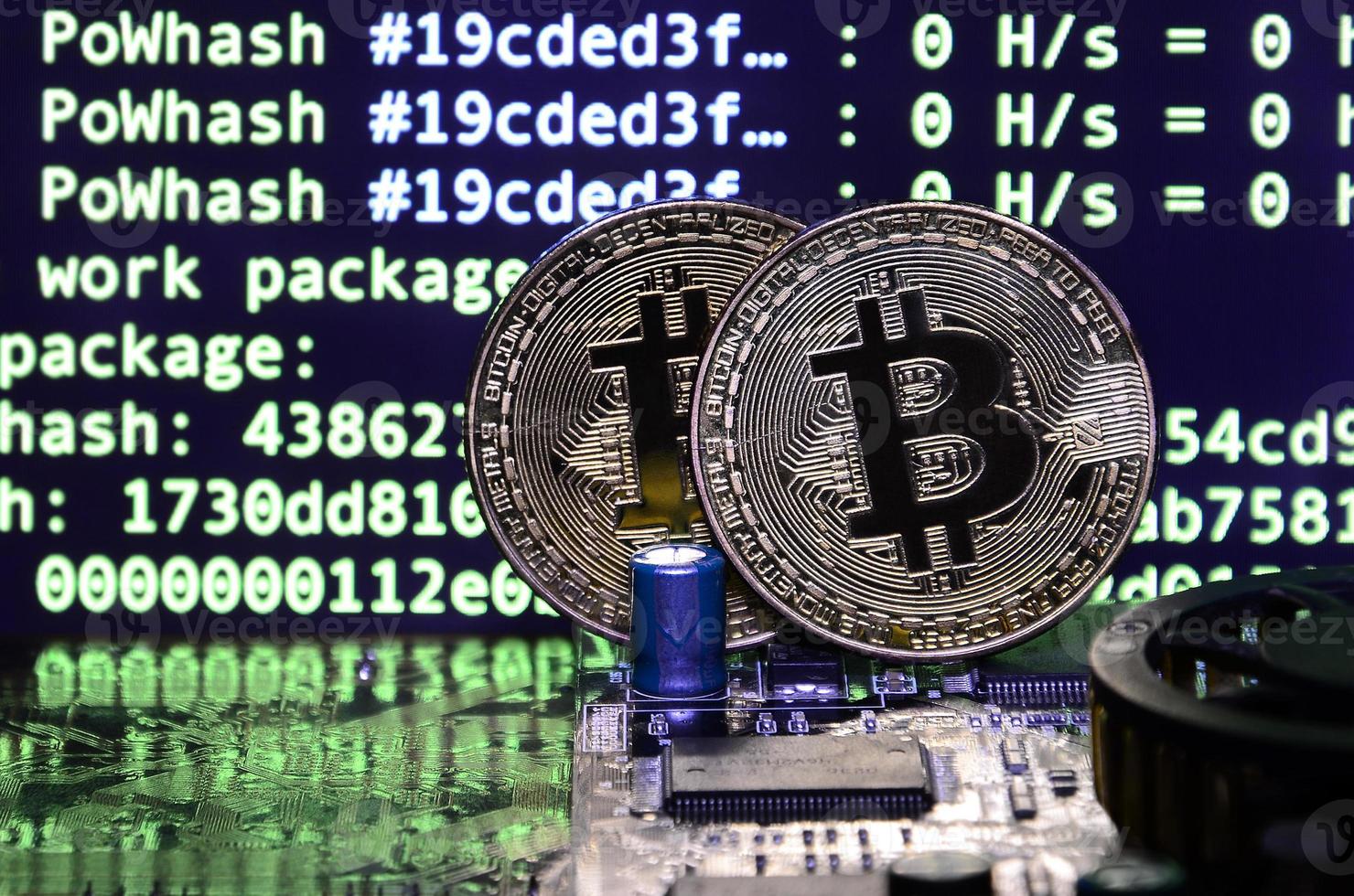 Two bitcoins lies on a videocard surface with background of screen display of cryptocurrency mining by using the GPUs photo