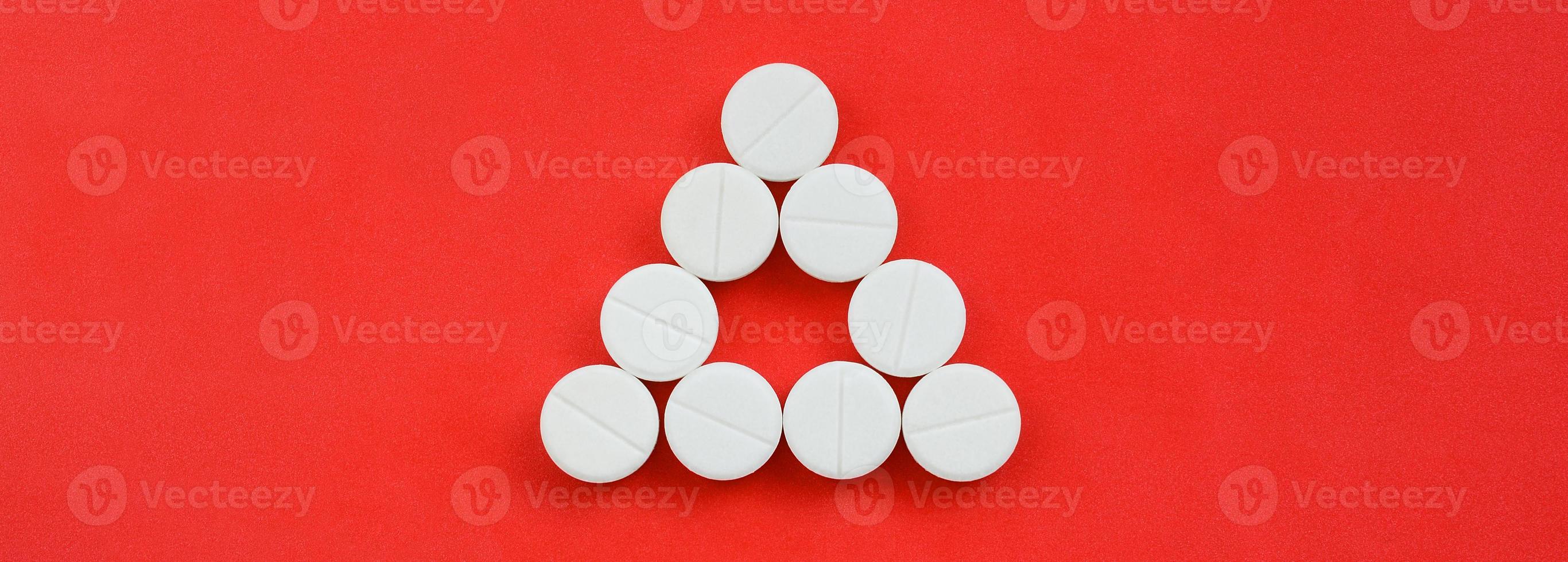 Several white tablets lie on a bright red background in the form of an even triangle. Background image on medicine and pharmaceutical topics photo