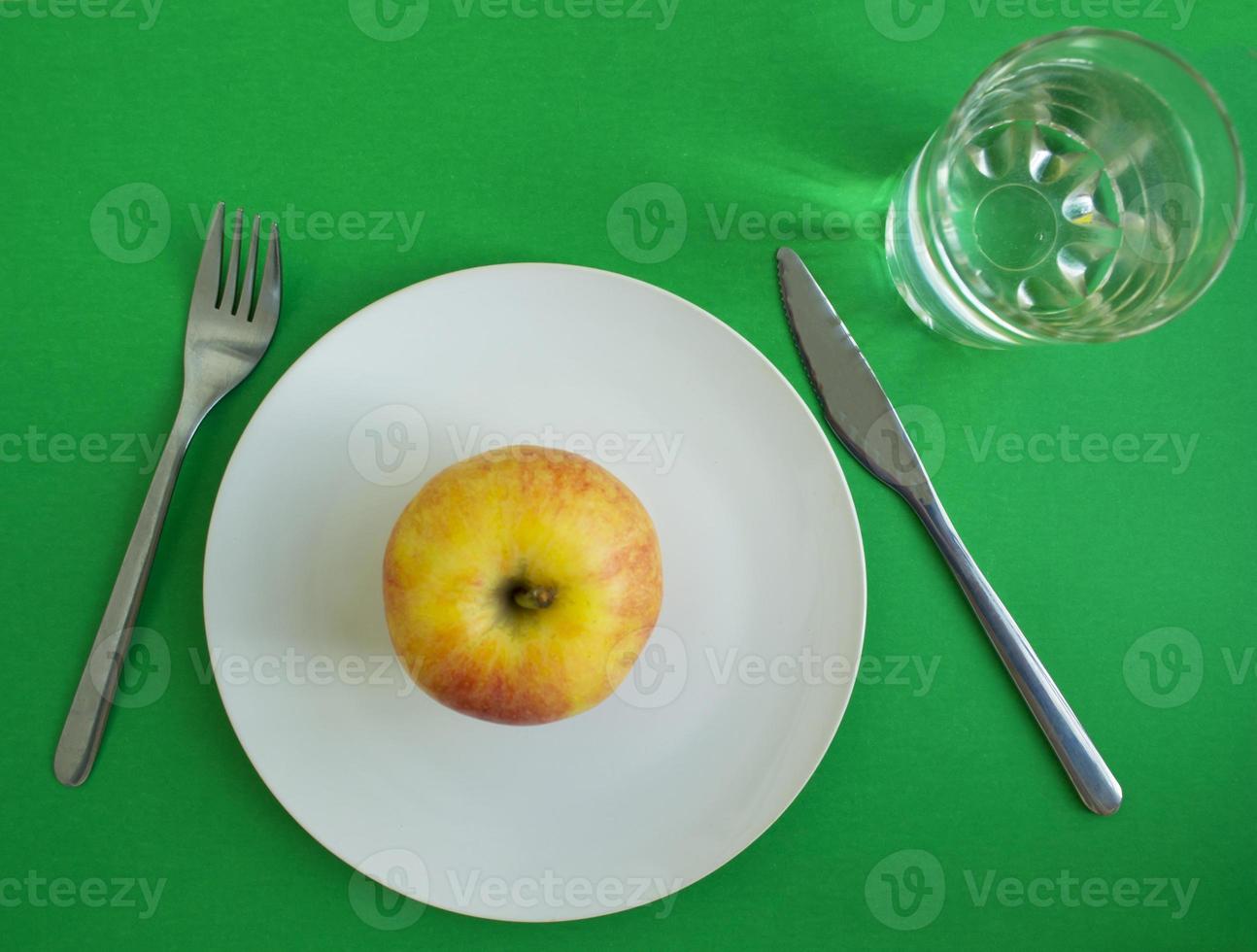 una manzana en un plato, un tenedor y un cuchillo, un vaso de agua foto