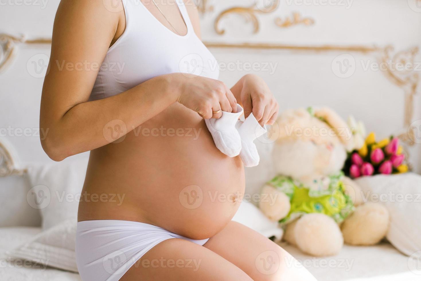 una mujer embarazada sostiene botines blancos en sus manos. una