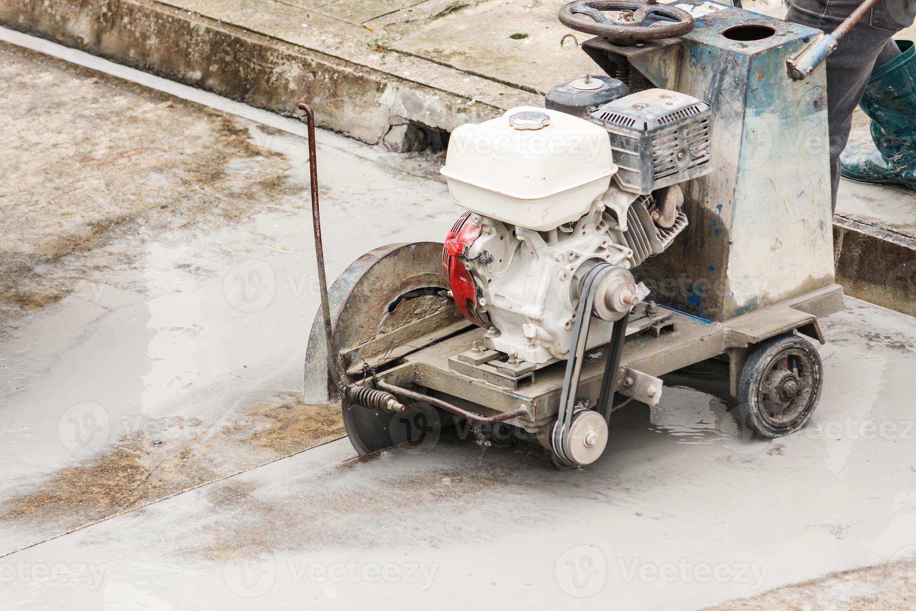 Worker using diamond saw blade machine cutting concrete road at