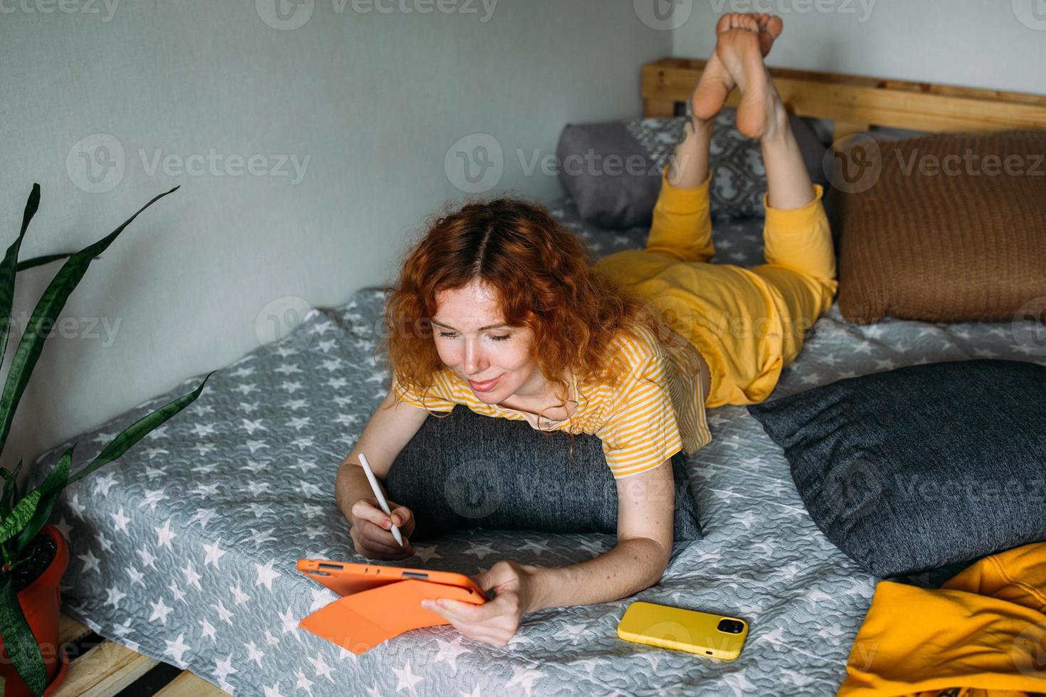 Woman working from home on bed using graphics tablet for design and drawing photo
