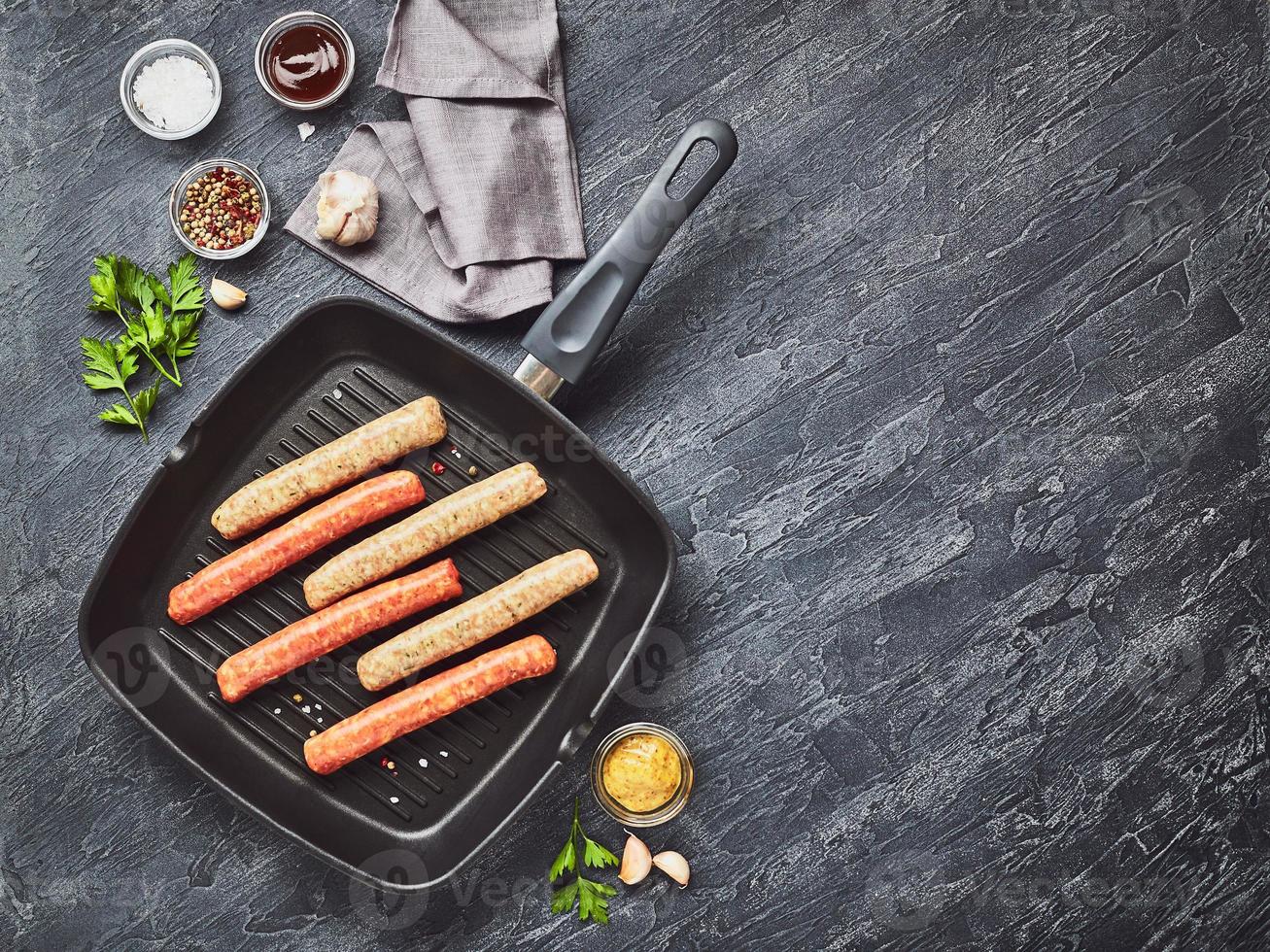 Raw meat sausages on square grill pan, with herbs and spices. Top view photo