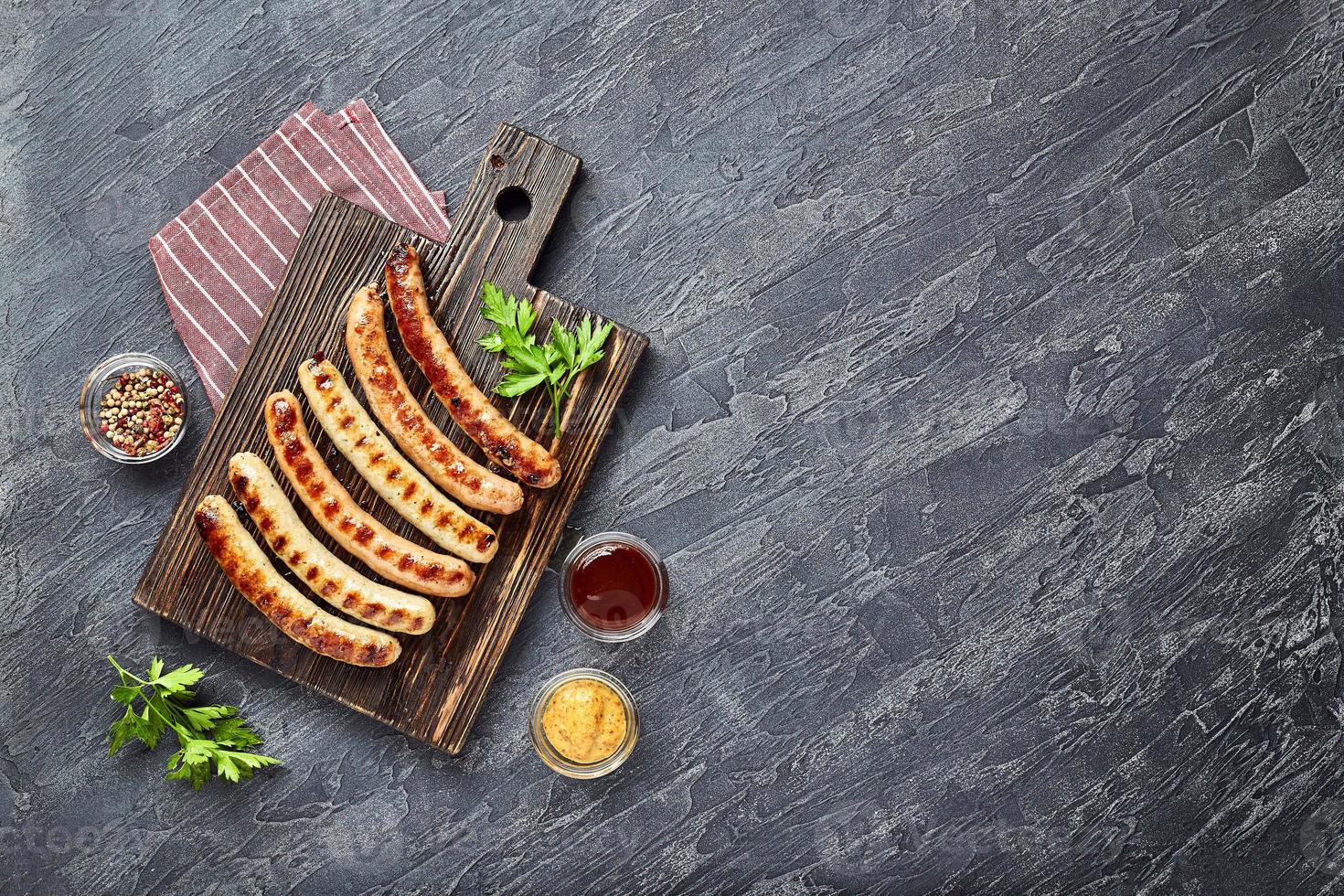 sabrosas salchichas de cerdo a la parrilla con especias y hierbas en tabla de cortar de madera foto