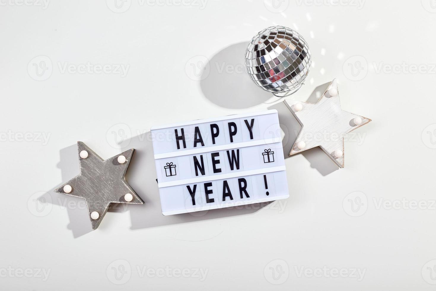 inscripción de caja de luz feliz año nuevo, bola de discoteca espejada y decoraciones de estrellas de madera foto
