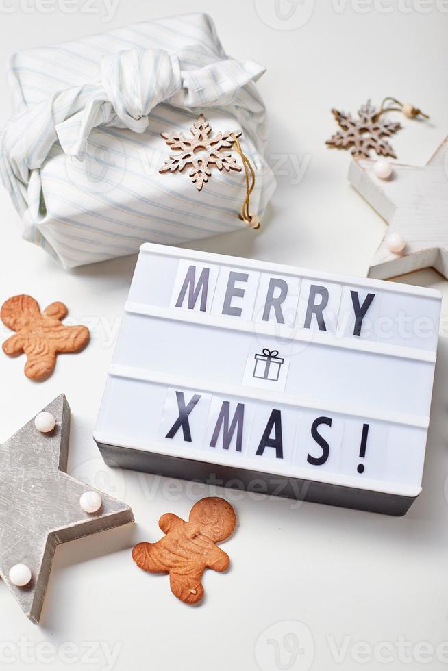 Light box inscription Merry Christmas, gifts in Japanese furoshiki style and gingerbread cookies photo