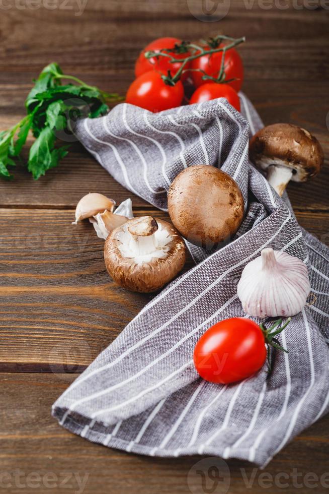 Tomatoes, garlic, champignons, parsley, pepper shaker, forks and napkin on wooden background photo