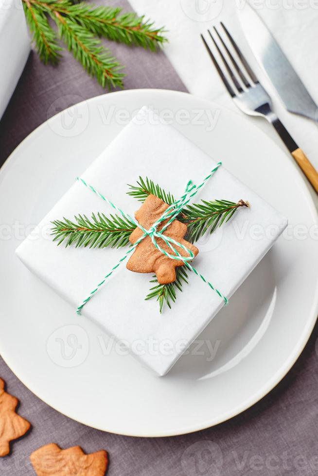 mesa festiva de navidad, plato con regalo decorado con ramitas de abeto y pan de jengibre foto