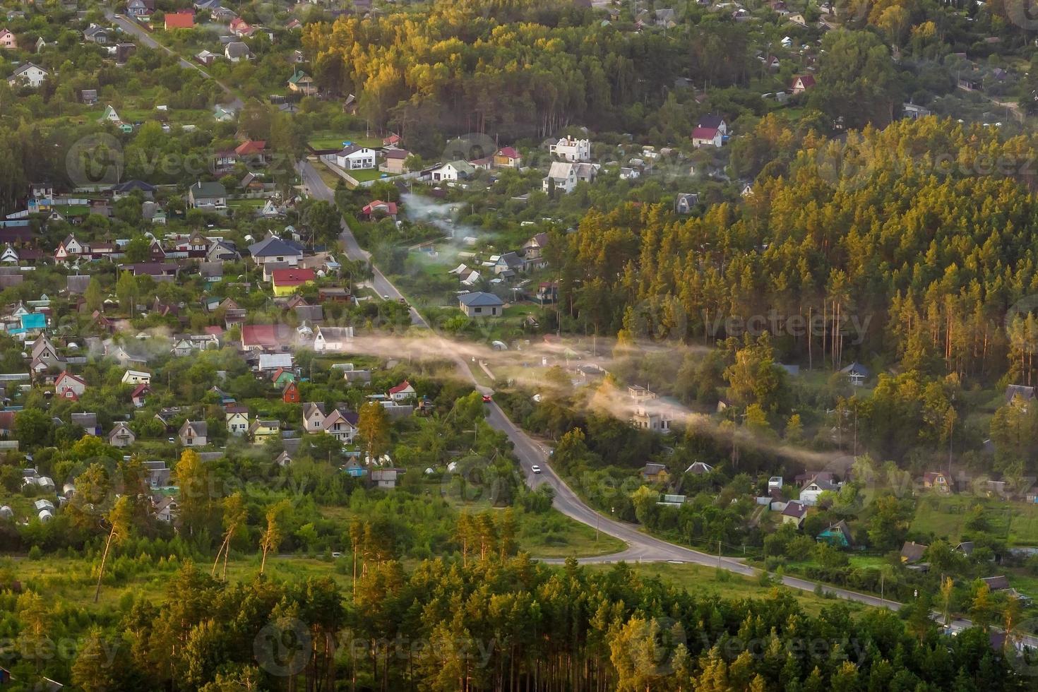 aerial panoramic view of green village with houses, barns and gravel road in forest photo