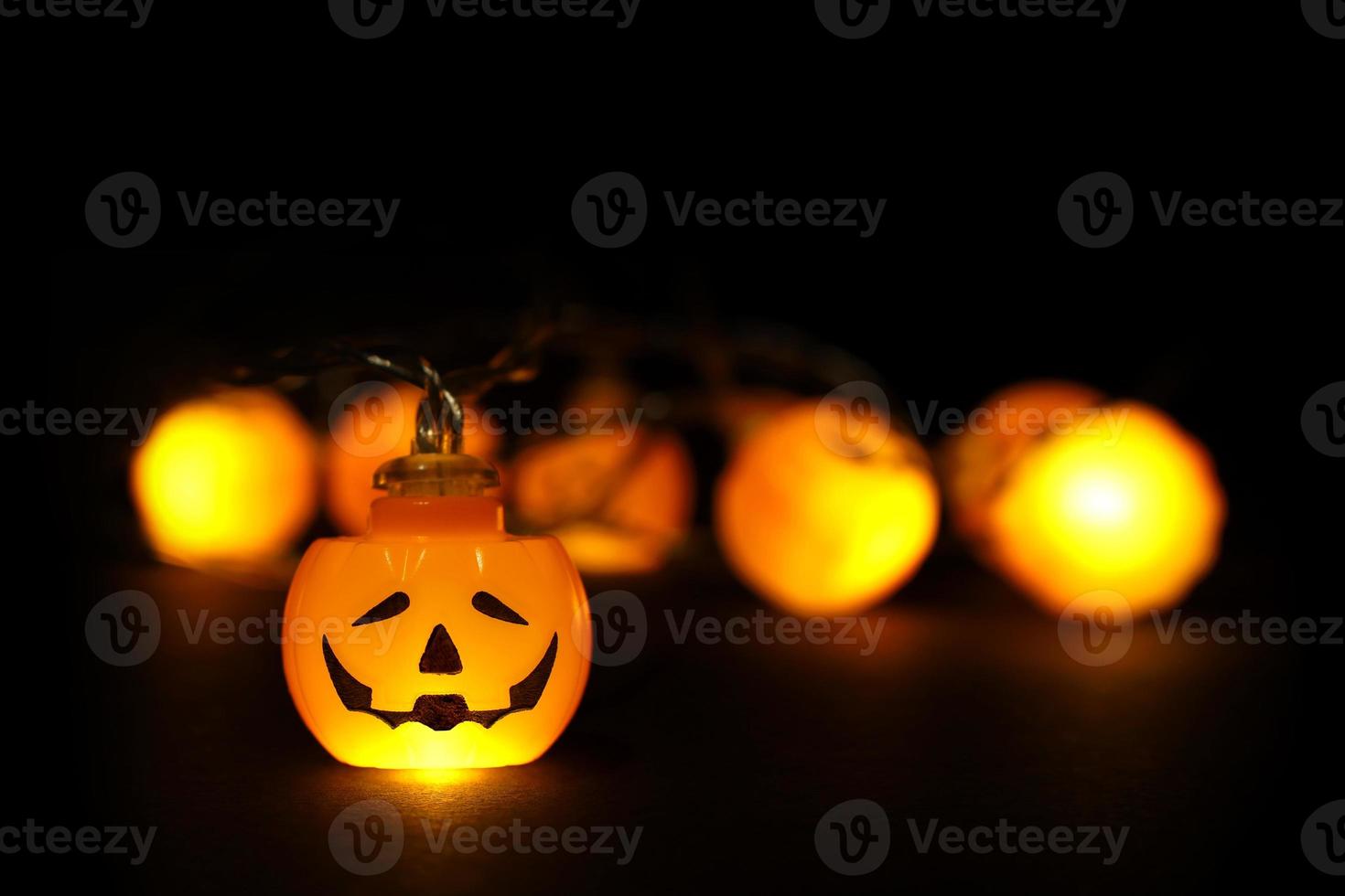 Garland lights of glowing halloween orange pumpkins with copy space above and below on black background. Blurred bokeh lights, one pumpkin face focused, close up. Festive holidays Halloween concept. photo
